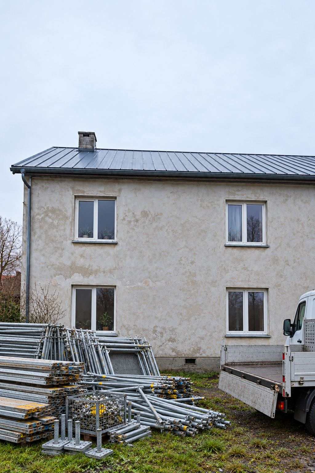 Sastatņu detaļas izkrautas zālienā pie mājas, blakus kravas auto